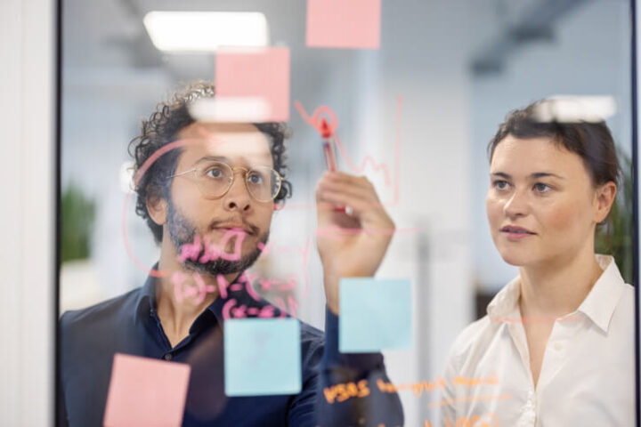 Man en vrouw bekijken ict-processtappen op plakbriefjes aan doorzichtige wand