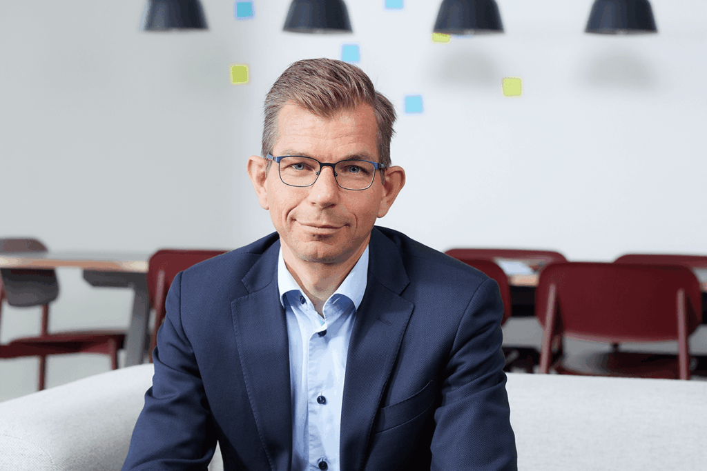 Matthijs van den Berg, directeur Kennis bij de Onderwijsinspectie, is tot zijn bovenlijf zichtbaar, draagt een bril en pak en zit op een bank.