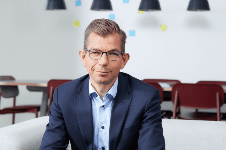 Matthijs van den Berg, directeur Kennis bij de Onderwijsinspectie, is tot zijn bovenlijf zichtbaar, draagt een bril en pak en zit op een bank.