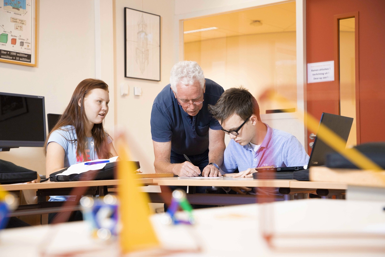 Een wiskundedocent van VSO Zeist geeft uitleg aan twee leerlingen