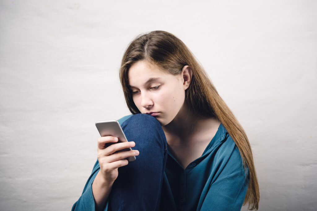 Afbeelding van een tienermeisje dat zorgelijk haar telefoon bekijkt