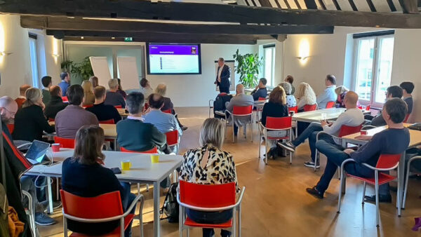 Bijeenkomst van het netwerk informatiemanagement. Mensen zitten in een zaal waar iemand spreekt.